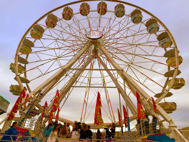 Large ferris wheel at an amusement park silhouetted against a warm sunset sky with mountain scenery in the background. Scenic travel and leisure concept capturing golden hour light and dramatic clouds.