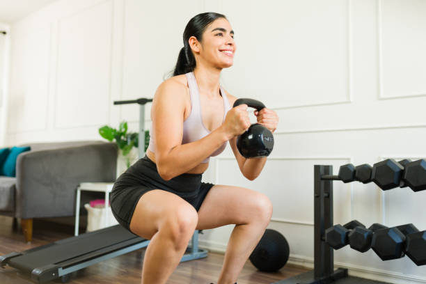 istock Athletic woman smiling as she performs squats with a kettlebell during her home workout 2169637297
