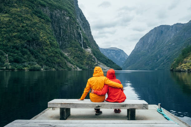 istock Happy couple dressed in bright windproof jackets sitting and hugging on bench on the Norwegian NÃ¦rÃ¸yfjord bank in Gudvangen, Norway. Traveling, beauty in Nature and relations concept. 2169649059