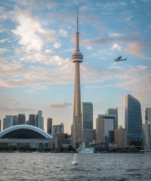 The Toronto city skyline as seen from Centre Island at dusk.  An airplane is flying into the frame prior to landing at Billy Bishop Airport.