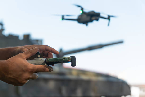 man with a uav control panel in his hands, a drone flying above the tank in the background in nature. help of reconnaissance drones in modern warfare. - avião sem piloto - fotografias e filmes do acervo