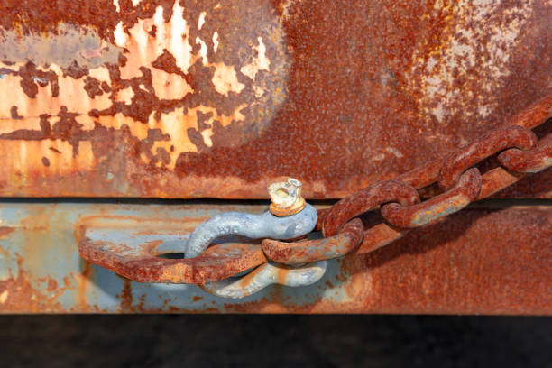 Photograph of an old D Bolt shackle connected to a rusty chain on a large brown and rusty metal storage container.