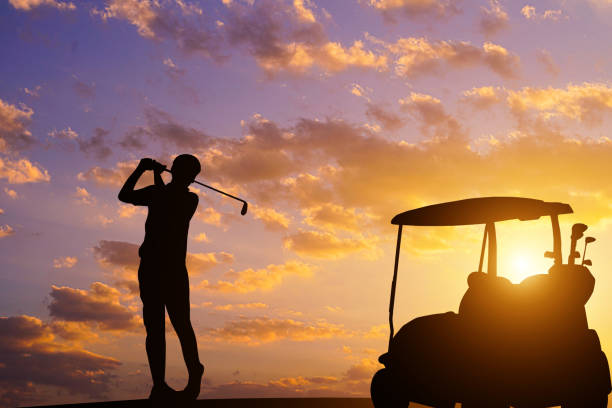 Golfers' hit golf ball toward the hole at sunset silhouetted. Golden morning sky in winter, misty high mountain background.