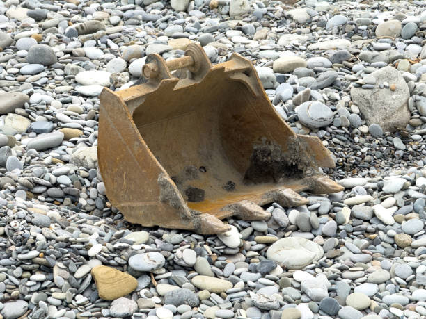 Excavator bucket on stone pebbles on the seashore.