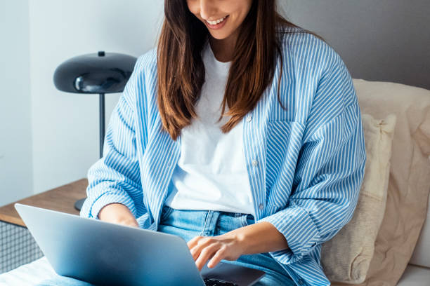 istock Young woman sitting on her bed, smiling while chatting online with friends using a laptop and wireless internet. A passionate technology enthusiast, she balances remote work, socializing, and modern digital communication 2169685989