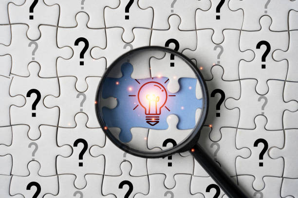 Glowing light bulb inside magnifier glass among question mark on jigsaw puzzle for focus and concentrate of creative thinking idea and problem solving concept.
