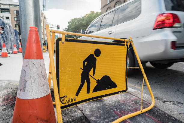 Sydney, NSW, Australia, February 19th 2024. A construction warning sign shows a worker digging alongside a traffic cone, with car in the backdrop.
