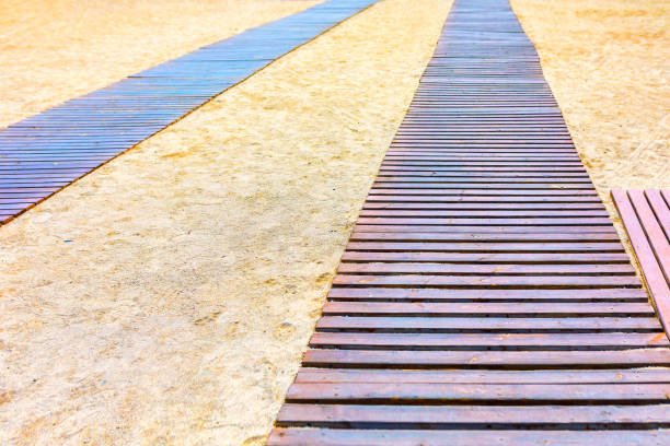 Wooden walkway is on a sandy beach. Wooden path stretches across the sandy beach, leading towards the ocean
