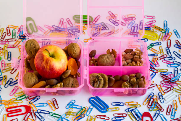 Pink,hard plastic food box for school children designed on colorful paper clips.Apple,dry fruits and mixed nuts.