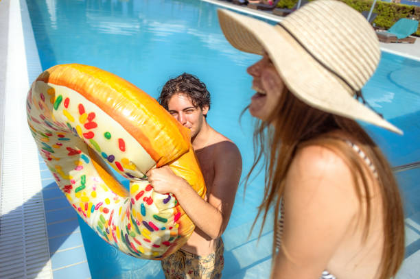 Girl with a sun hat standing with teenage boy near pool and smiling while talking