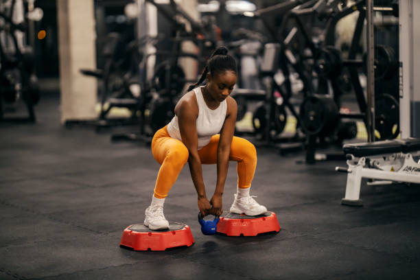 A fit black sportswoman doing deep squats with kettle bell at gym.