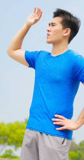closeup asian man standing outdoor feeling summer hot raise hands up cover the sunshine his eyes closed fearing sunlight
