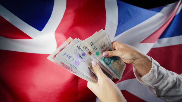 UK flag background. Woman counting GBP money pounds sterling. Credits, raising tariffs in Great Britain, traveling costs, financial concept. UK flag background. Woman counting GBP money pounds sterling. Credits, raising tariffs in Great Britain, traveling costs, financial concept. High quality british currency stock pictures, royalty-free photos & images