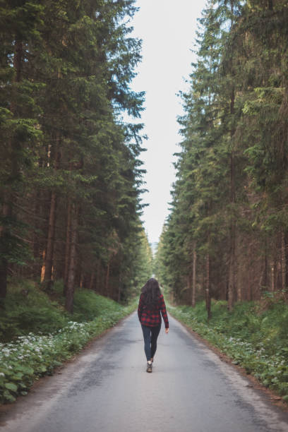 istock Young woman in a red plaid shirt walking down a peaceful, tree-lined forest road, embracing the tranquility and beauty of nature, symbolizing freedom and a journey of self-discovery 2169727398