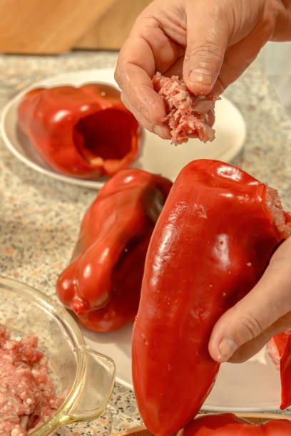 Cook stuffs a seeded red bell pepper with raw minced meat. Close-up