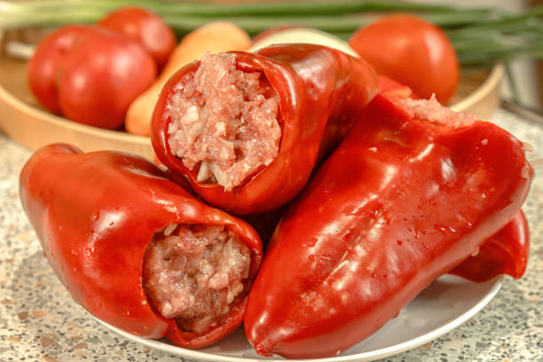 Red bell pepper stuffed with minced meat on a kitchen table with vegetables in the background. Close-up