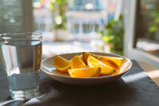 orange mono diet. peeled orange slices on plate and glass of clean water in glass on table, in rays of sun