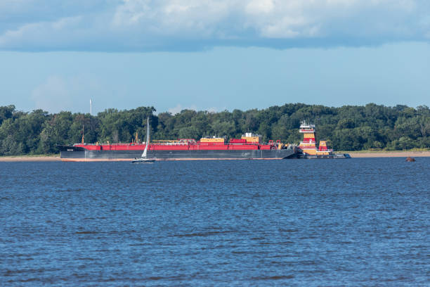 South Amboy, New Jersey - August 21, 2024: A tugboat assists a barge in the Arthur Kill in South Amboy, New Jersey, surrounded by lush greenery on a sunny summer day