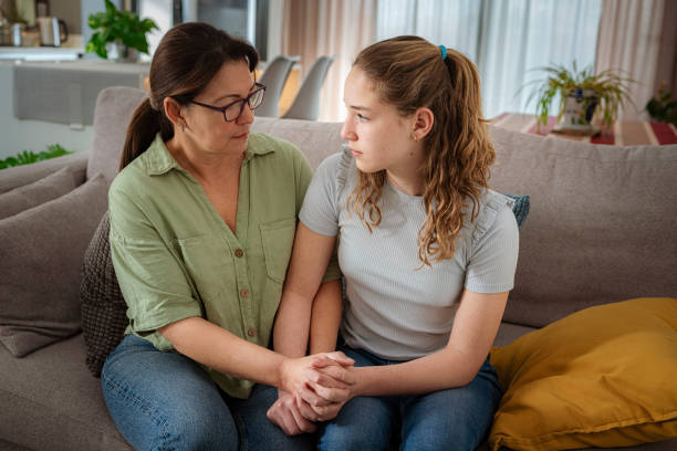 istock Mother and daughter sitting on sofa holding hands and talking about adolescence problems 2169755061