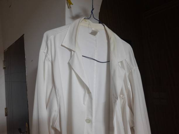 istock white lab coat on a blue hanger, with a white wall and a brown door in the back 2169757589