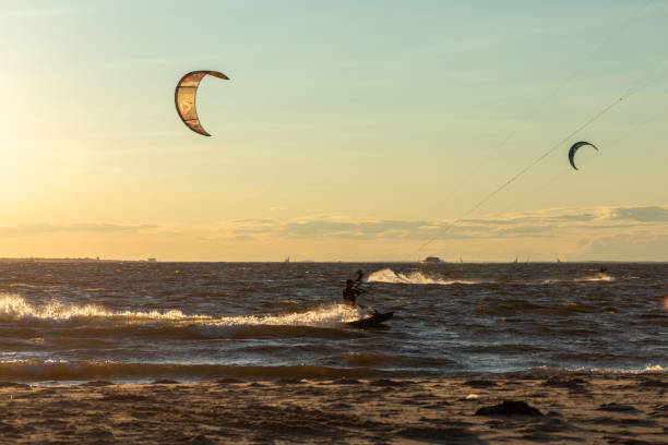 Seascape on a lazy day. There are waves, blue sky with white clouds, a breakwater made of wooden logs. A figure of a man riding a kiteboard is visible. Landscape.