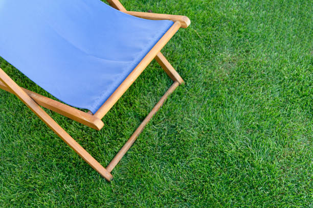 Deck chair with blue fabric on green grass background. Top view.