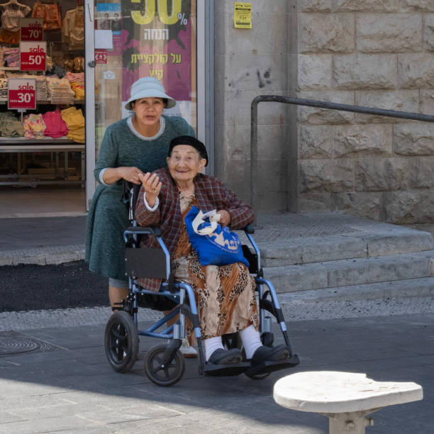 Jerusalem, Israel - July 2nd, 2024: A portrait of a senior citizen on a wheelchair and her personal caregiver.