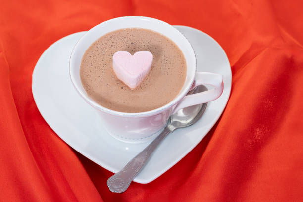 A cup of hot chocolate with a heart shaped marshmallow - red satin background
