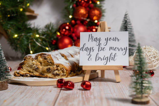 istock Greeting card with message MAY YOUR DAYS BE MERRY AND BRIGHT congratulations. Christmas Stollen in Christmas lights and decoration. Traditional sweet fruit loaf with icing sugar festive pastry dessert. Holiday baking food 2169810082