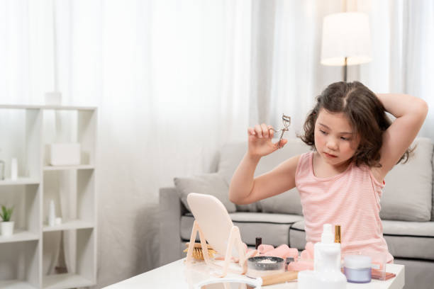 istock curling eyelashes. Happy children sit in front of a mirror makeup on face Advertisement, lifestyle , cosmetics, makeup accessories, beauty activity, beautician, talent, love beauty 2169817625