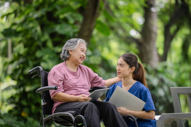 istock Elderly woman engaging with a nurse while using a tablet, sharing a joyful moment in a serene park setting. 2169818169