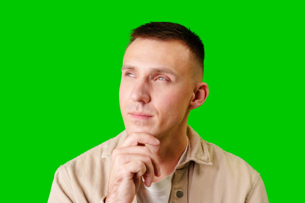 istock Young Man in Casual Attire Posing Thoughtfully Against a Bright Green Background 2169825617