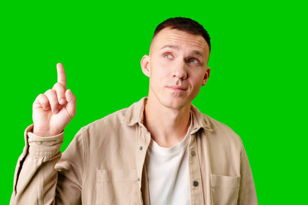 istock Young Man Pointing Upward While Smiling Against a Bright Green Background 2169826566