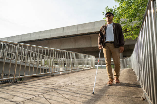 istock Young blind man walking in city with walking stick. Visually impaired man difficult to traveling on the road wearing sun glasses Cross the road cross the footbridge 2169828823