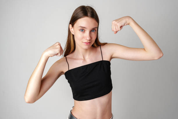 istock Young Woman Flexing Muscles in Black Top Against White Background 2169829059