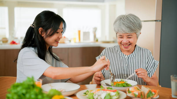 Young Asian woman bringing some healthy food to the dining table to eat with her mother. stock photo