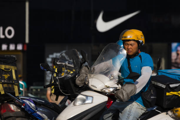A delivery driver on a motorcycle is en route to deliver food in front of a Nike store on September 1, 2024 in Chongqing, China. The Chongqing Meteorological Observatory continued to issue a red high-temperature warning, marking the 12th consecutive day of such an alert.