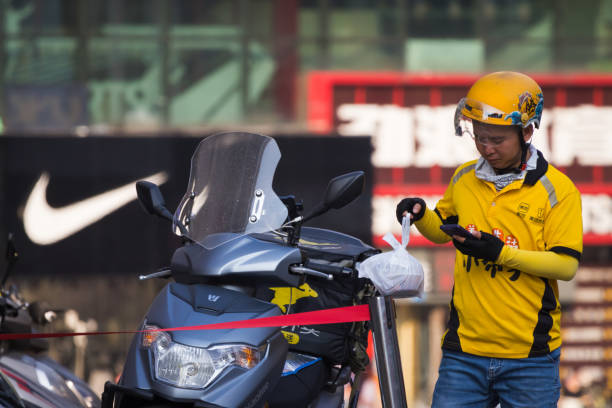 A Meituan delivery driver checks his phone while standing next to his motorbike in front of a Nike store on September 1, 2024 in Chongqing, China. The Chongqing Meteorological Observatory continued to issue a red high-temperature warning, marking the 12th consecutive day of such an alert.