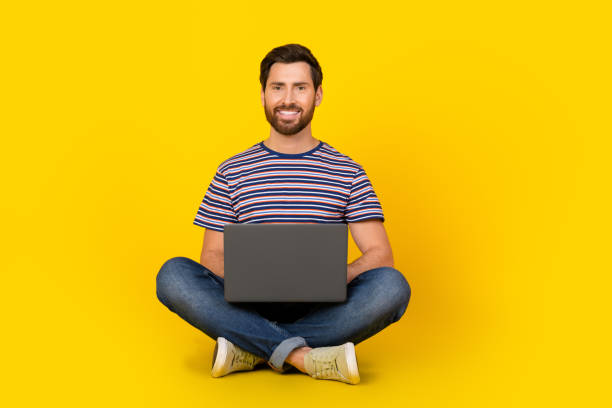 istock Photo of young modern working guy with netbook likes using online service for eshopping isolated on yellow color background 2169833910