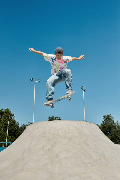 A young man in bright clothes does tricks on a skateboard in a sunny park