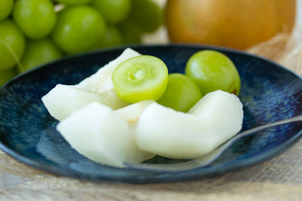 Fruits and berries are scattered from a paper bag. Melon, peach, plum, raspberry, blueberry are scattered on the table.