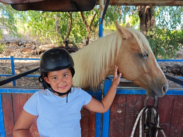 detail of four years old blonde girl, with equestrian cap, riding a horse in a forest