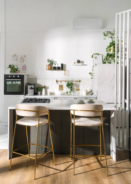Modern kitchen with minimalist decor featuring plants and golden bar stools in a bright space