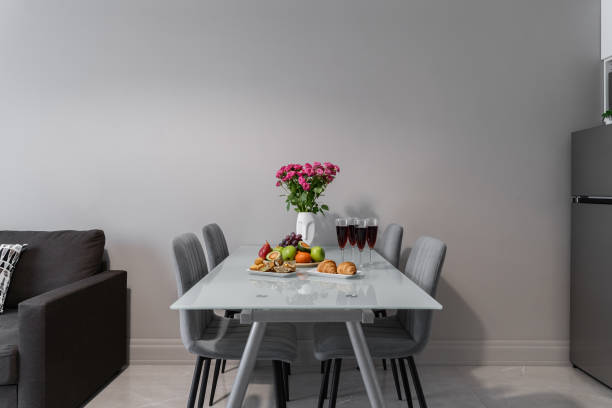 istock design of modern kitchen, living room. glass table, gray chairs, sofa. white vase with roses, glasses with red wine, croissants, fruits, grapes, apples, avocados, pears, sweets. beautiful dinner. 2169849708