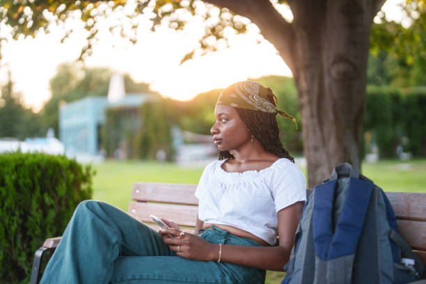 istock Young adult student is using mobile phone on a park bench. 2169852118