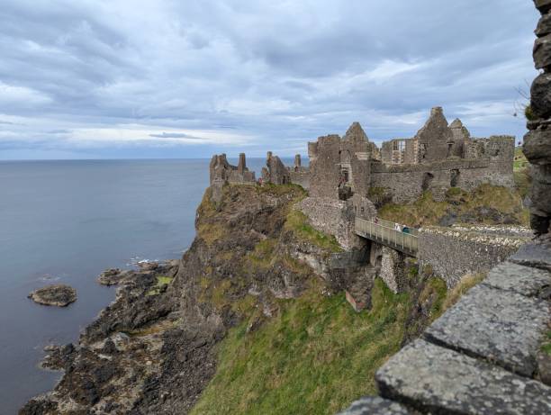 istock Dunluce Castle on the cliffs edge with a wooden bridge and grey skies 2169862488
