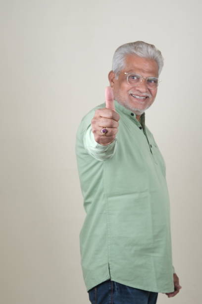 Indian Asian Elderly Sikh Man Sitting at Table on White Background, Resting, Thinking, Showing Thumbs Up, Pointing, or Displaying Confused Expression