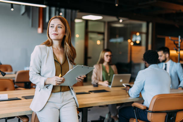 Confident businesswoman and her team. Portrait of beautiful smiling businesswoman with her colleagues during a meeting in office board room. Successful team leader and her team working in background. group of people standing together stock pictures, royalty-free photos & images