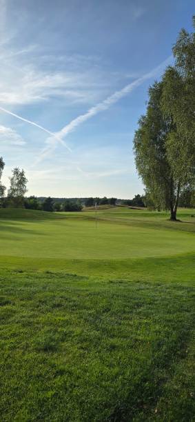 istock golf course with a green area, a hole, and a flagstick, surrounded by trees under a clear sky. 2169870609