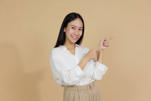 istock Smiling Woman Pointing to the Side with Both Hands, Beige Background 2169871448